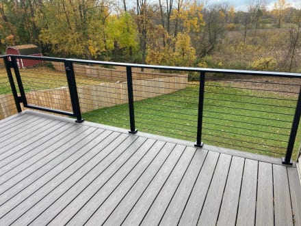 Black posts and top rail with cable infill along a gray composite deck overlooking a fenced lawn in autumn.