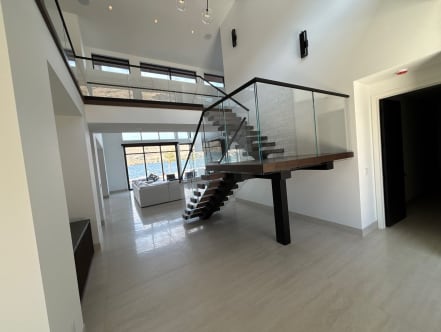 Dark wood floating stair with a post-supported landing, frameless glass and black top cap, lake view beyond