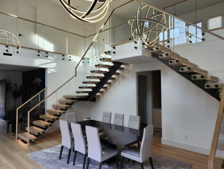 Black-stringer FLIGHT Mono stairs with oak treads and standoff-pin glass railing overlook a formal dining room.