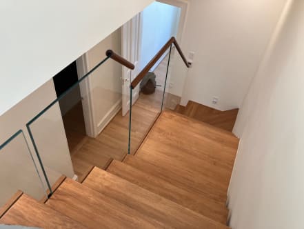 Frameless glass with a walnut handrail along a wood switchback stair seen from above.