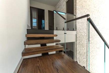 A few stained oak floating treads with glass railing rise to a wood landing beside a stone wall.