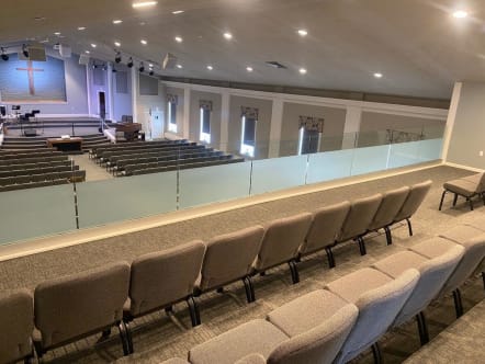Frameless glass railing lines a sanctuary balcony above rows of upholstered seating.