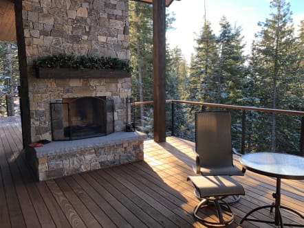 Black Onyx rod railing with wood cap rail around an ipe deck beside a stone fireplace among snowy pines.