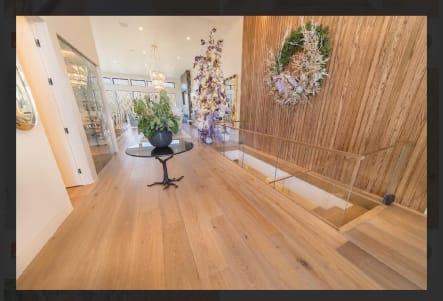 Frameless glass railing with a wood cap rail surrounds a stairwell opening in a wide white oak hallway.