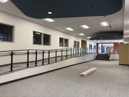 Long accessible ramp lined with black-post glass railing and handrails in a commercial corridor