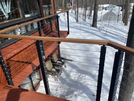 Black slim posts and wood cap cable railing along a red deck above a snowy yard.