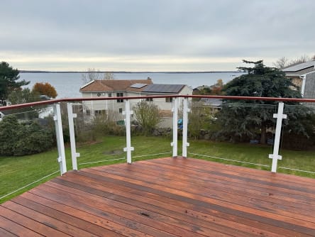 White posts with glass infill and a curved Ipe cap rail edge a wood deck facing the water.