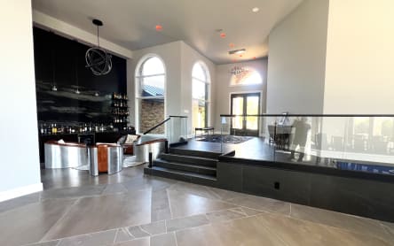 Frameless glass railing on talon spigots wraps a raised platform in a dramatic home bar