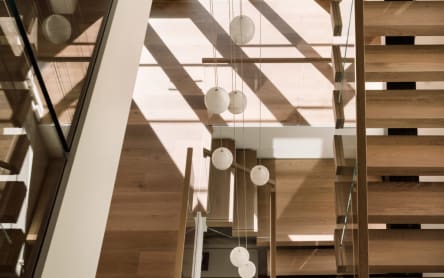 Overhead view of wood floating treads and glass railings stacked through a multi-level stairwell with globe pendants.