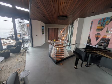 Base rail glass with a walnut cap wraps a lit stair opening beside a grand piano and lake view