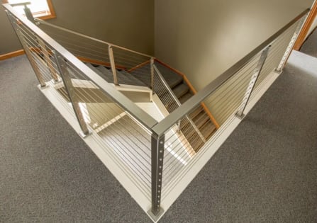 Overhead view of stainless steel posts and cable infill wrapping a carpeted stair opening.