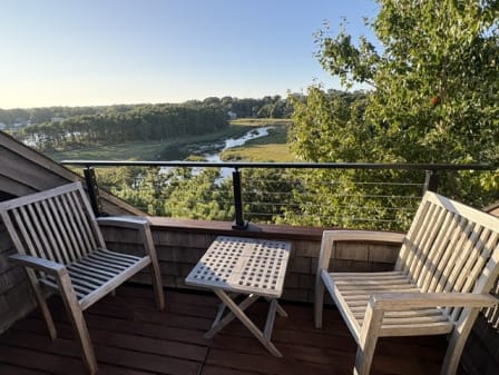 Black cable railing on a compact balcony with teak chairs overlooking a salt marsh.
