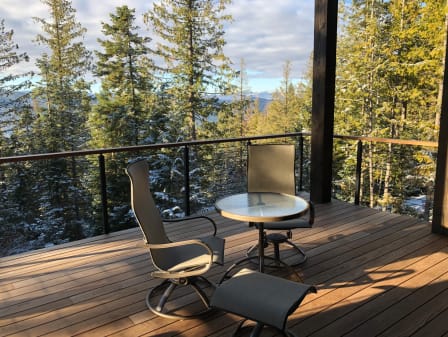Black rod railing with wooden cap around an ipe deck with patio chairs overlooking a forested valley.