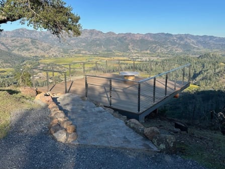 Stainless cable railing around a hillside deck reached by a stone path with mountain views.