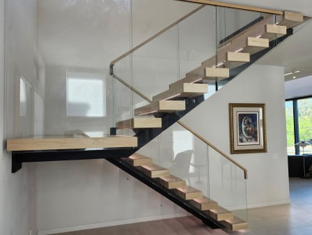 Light oak treads on a black mono stringer with frameless glass railing, wood handrail and LED lights.