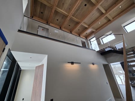 Frameless base rail glass with a wood cap lines an upper-floor balcony beneath a coffered wood ceiling