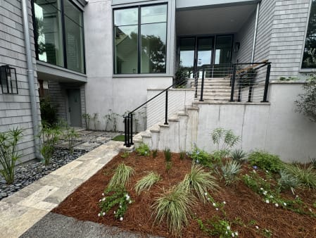 Black-post cable railing climbs concrete entry stairs beside fresh landscaping on a modern shingled home