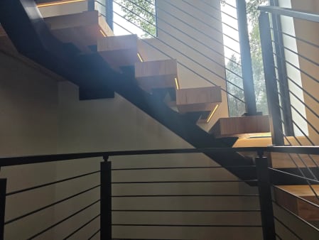 Floating stair with LED-lit treads above a black cable railing at the landing