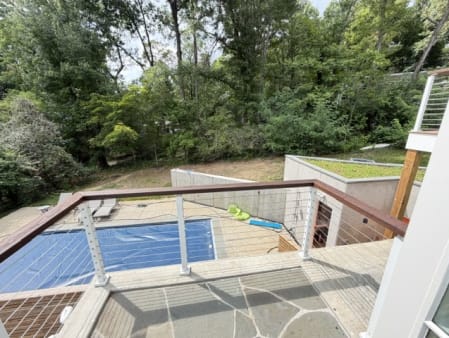 White-post cable railing with a dark wood top rail edges a flagstone terrace above a pool