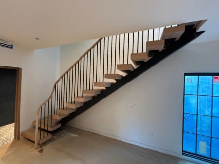 White oak floating stair on a black stringer with tapered black modern balusters and a sweeping curved oak handrail