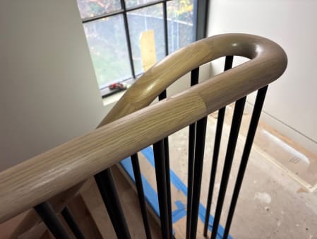 Close view of a smoothly curved white oak handrail over black modern balusters