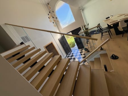 White oak floating stair with glass railing and wood handrail descending toward an arched entry
