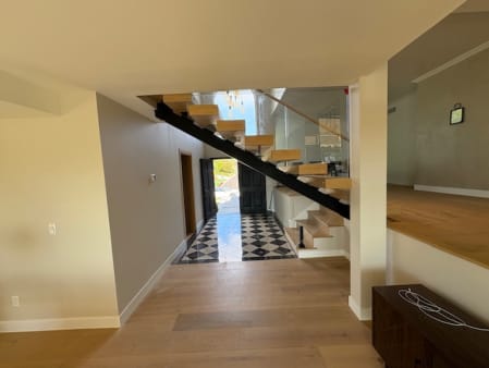 Black mono stringer floating stair with glass railing rising above a checkered entry floor