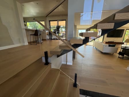 Floating oak treads on a black stringer with frameless glass and wood handrail in a bright great room