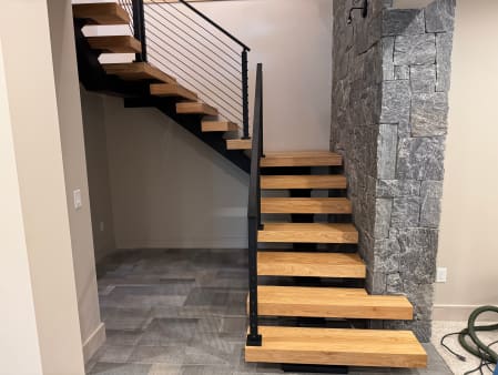 Thick oak floating treads with black cable railing turning beside a granite stone column