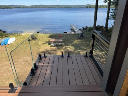 Frameless glass on jet black talons and cable railing frame a deck overlooking a lake beach and dock