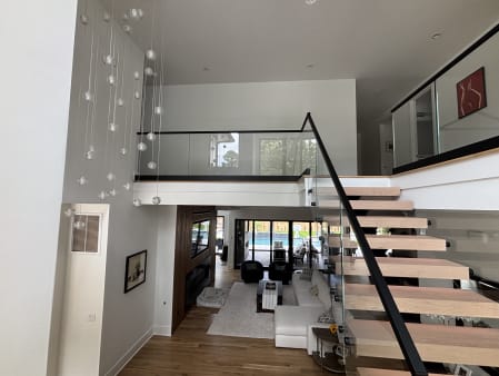 Floating white oak stair with glass railing rising to a glass-railed loft above a modern living room