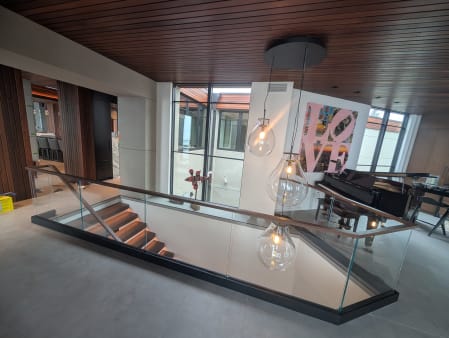 Frameless glass with walnut cap around a stair opening beneath glass pendants and a slatted walnut ceiling