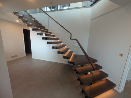 Walnut floating stair with glowing LED treads and frameless standoff glass with walnut handrail