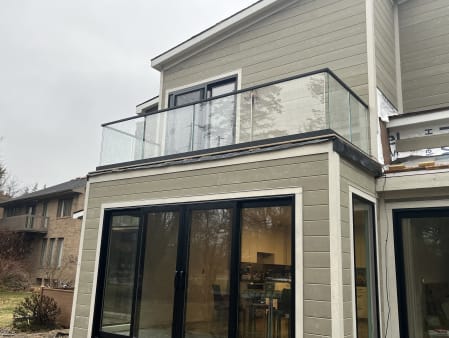 Frameless base rail glass balcony with a black cap on a gray-sided home
