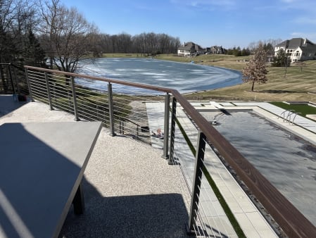 Cable railing with a wood top rail on a terrace overlooking a pool and frozen pond