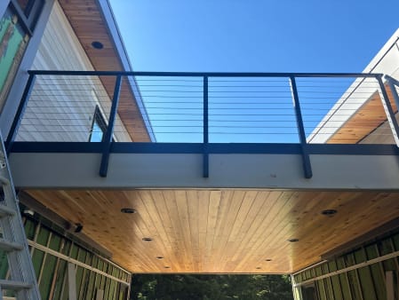 Black cable railing on a covered bridge balcony with a cedar ceiling against blue sky