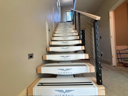 Floating stair in clean Viewrail tread covers with black cable railing and maple handrail