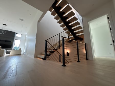 Black mono stringer floating stair with LED-lit treads and black cable railing in an open hall