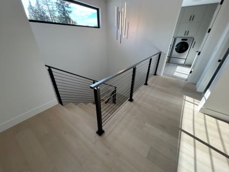 Black-post cable railing wraps a stair opening on pale oak floors under a clerestory window