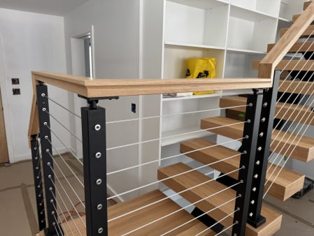 Black cable railing posts and a mitered red oak handrail at a floating stair landing