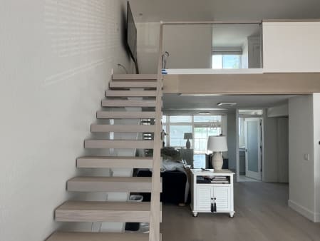 Whitewashed oak floating stair beside a frameless glass loft railing in a bright condo