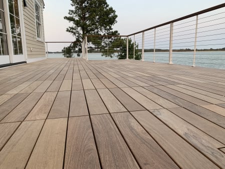 A wide hardwood deck overlooking a lake, edged by white-post cable railing with a wood cap rail.