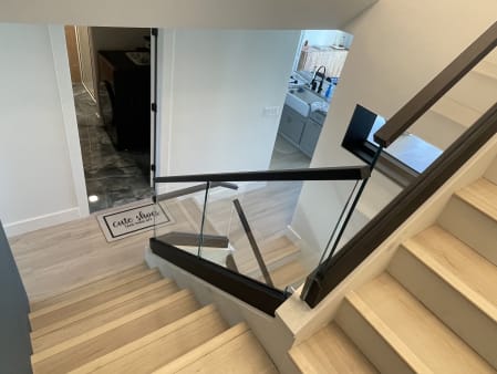View down a light oak stair lined with glass panels set in a black channel with a black top rail.