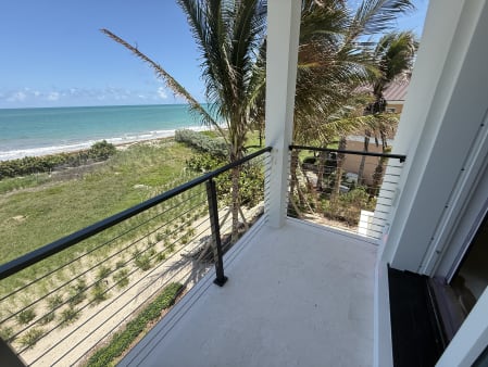 A black cable railing edges a white balcony overlooking dunes and turquoise ocean.