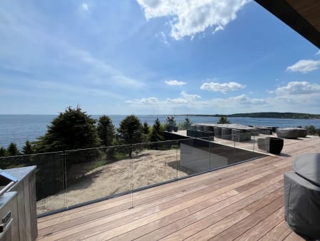 Long run of frameless glass railing on a hardwood terrace overlooking a bay under blue sky.