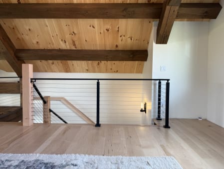 Black-post cable railing with wood newel guards a stair opening on a light hardwood loft.