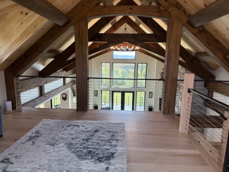 A cable railing with black top rail edges a loft overlooking a vaulted timber-frame great room.