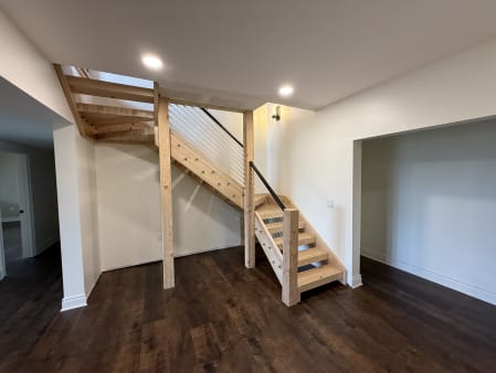 Cable railing with black handrail follows a natural wood open stair in a lower-level room.