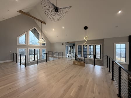 Black posts and handrail with horizontal cables enclose an open loft under a vaulted ceiling with tall gable windows.