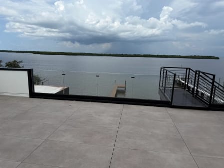 Frameless glass in a black base channel edges a tiled rooftop terrace overlooking a bay and boat dock.